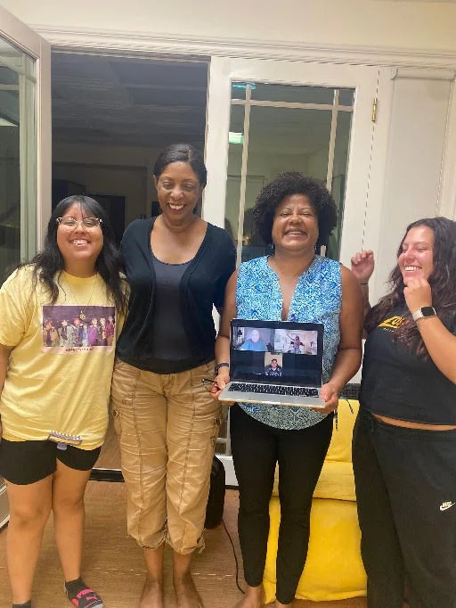 Members gathered around a laptop during a hybrid in-person and Zoom session